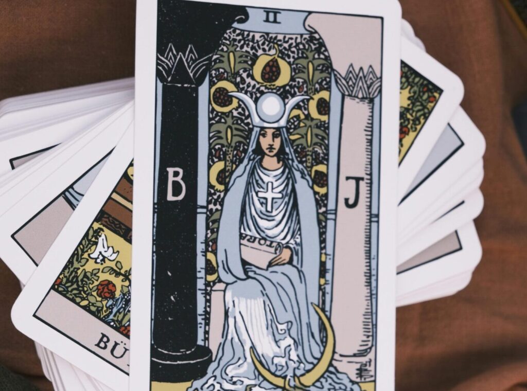 Deck of tarot cards spread on brown fabric with beads, emphasizing divination.