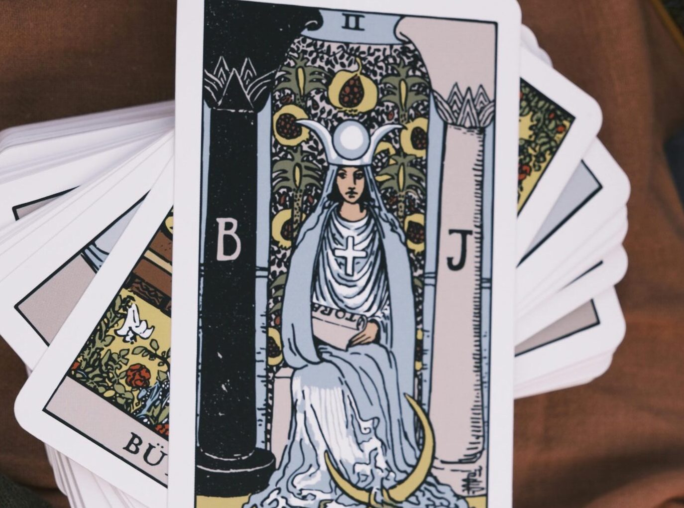 Deck of tarot cards spread on brown fabric with beads, emphasizing divination.